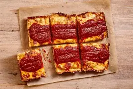 Close-up of Detroit-style pizza slice in a steel pan